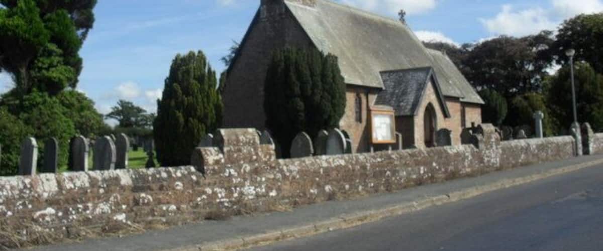 A church with a pointed steeple, surrounded by trees and a stone wall.