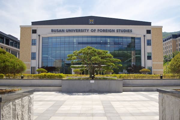 Le bâtiment de l’université des études étrangères de Busan, avec sa grande façade en verre et un arbre au centre de la cour.