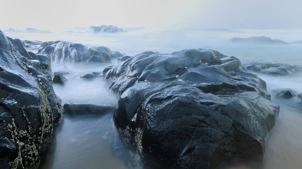 A rocky coastline with a misty sea and distant icebergs.