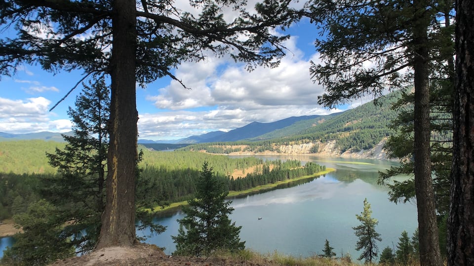 A lake surrounded by dense forest and mountains under a partly cloudy sky.