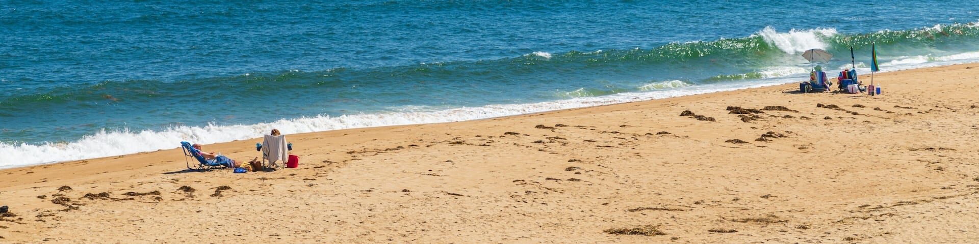 A sandy beach with ocean waves, a clear sky, and distant land.
