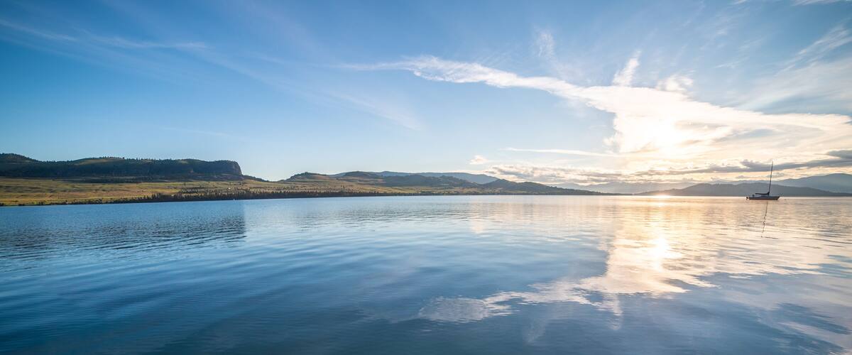 A calm lake with a sailboat, surrounded by rolling hills and a clear sky.