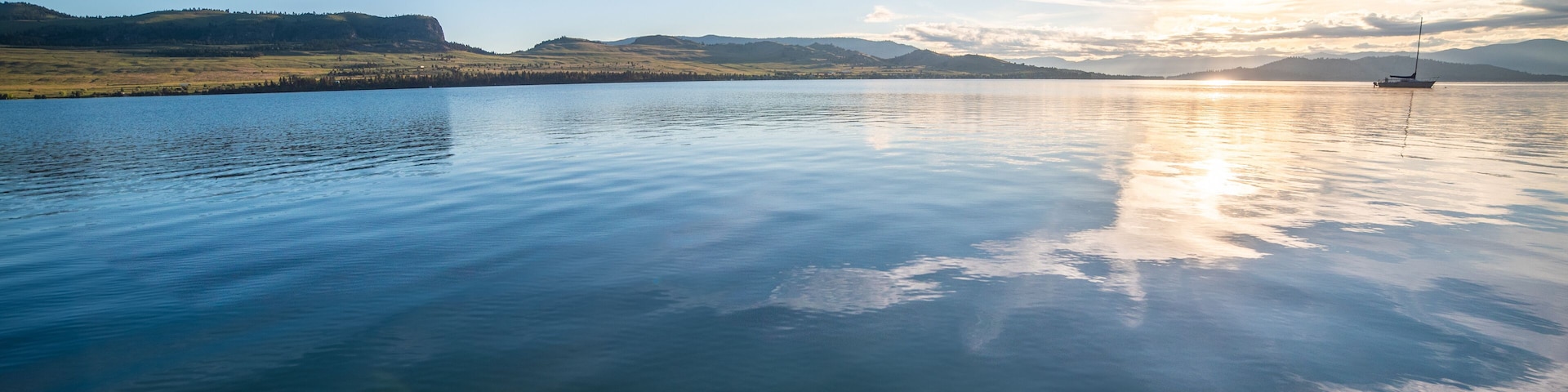 A calm lake with a sailboat, surrounded by rolling hills and a clear sky.