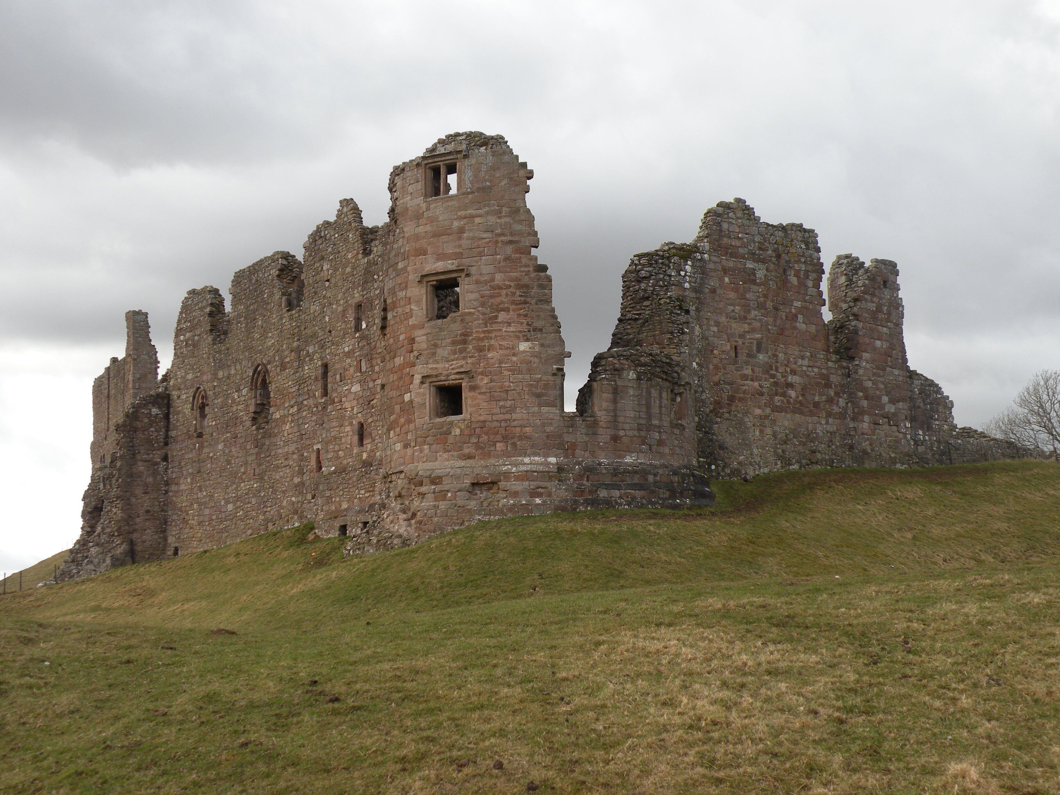 A large, historic stone castle on a grassy hill under a cloudy sky.