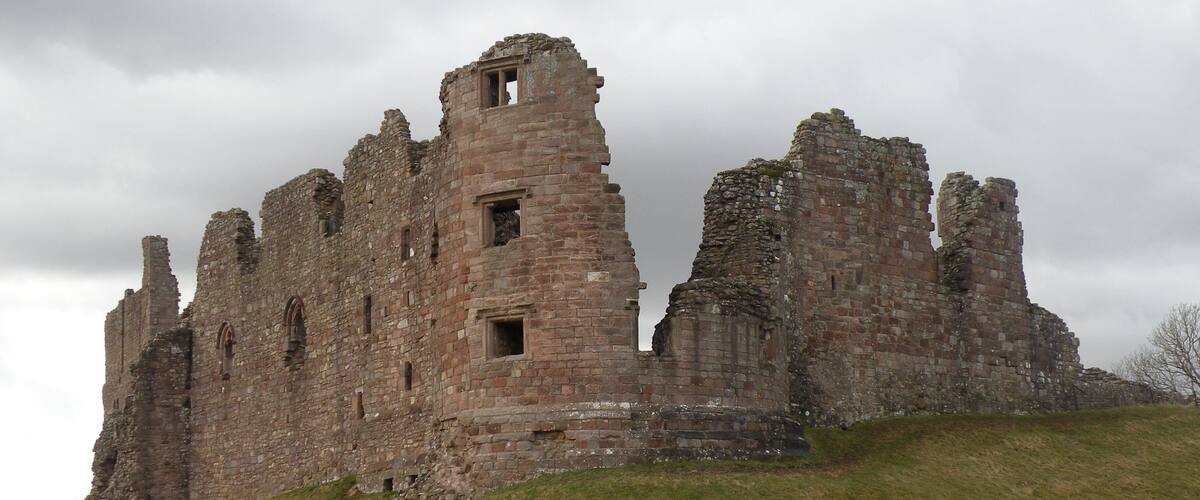 A large, historic stone castle on a grassy hill under a cloudy sky.