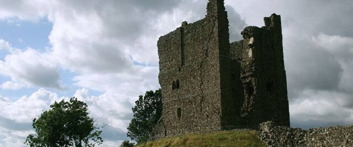 A historic stone castle ruin with a grassy hill and a cloudy sky.