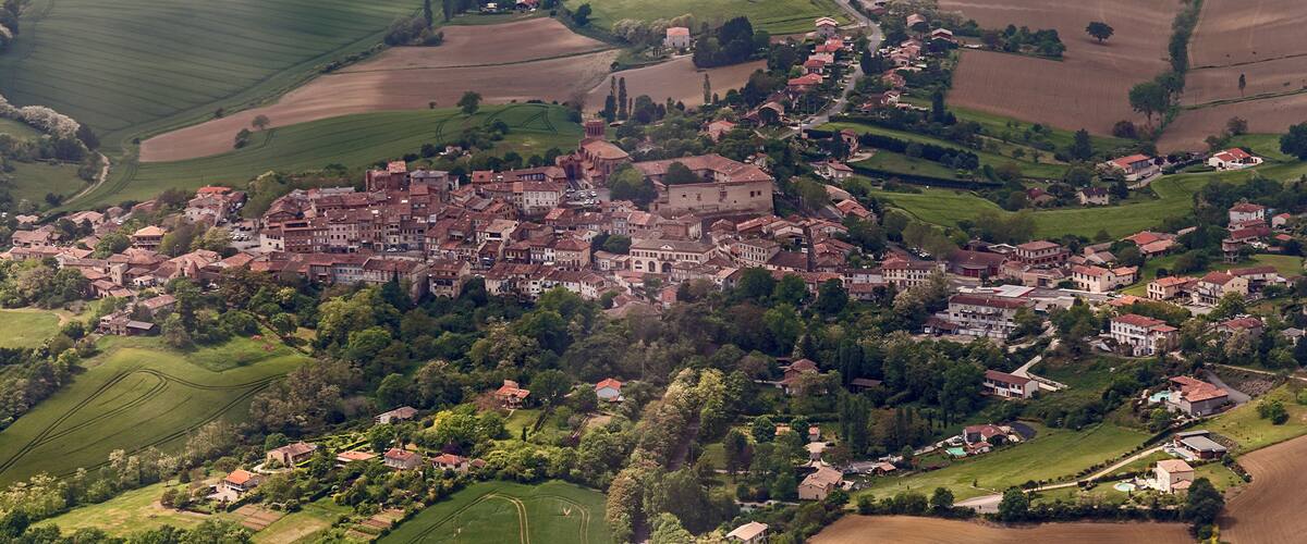 An aerial view of a historic town with dense architecture, rolling green fields, and a prominent church.