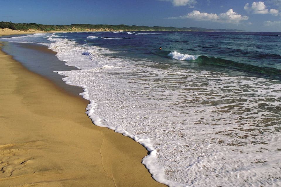 A sandy beach with waves crashing onto the shore and a clear sky.