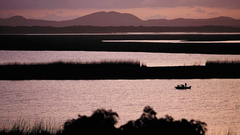 A calm lake with a boat and distant mountains.