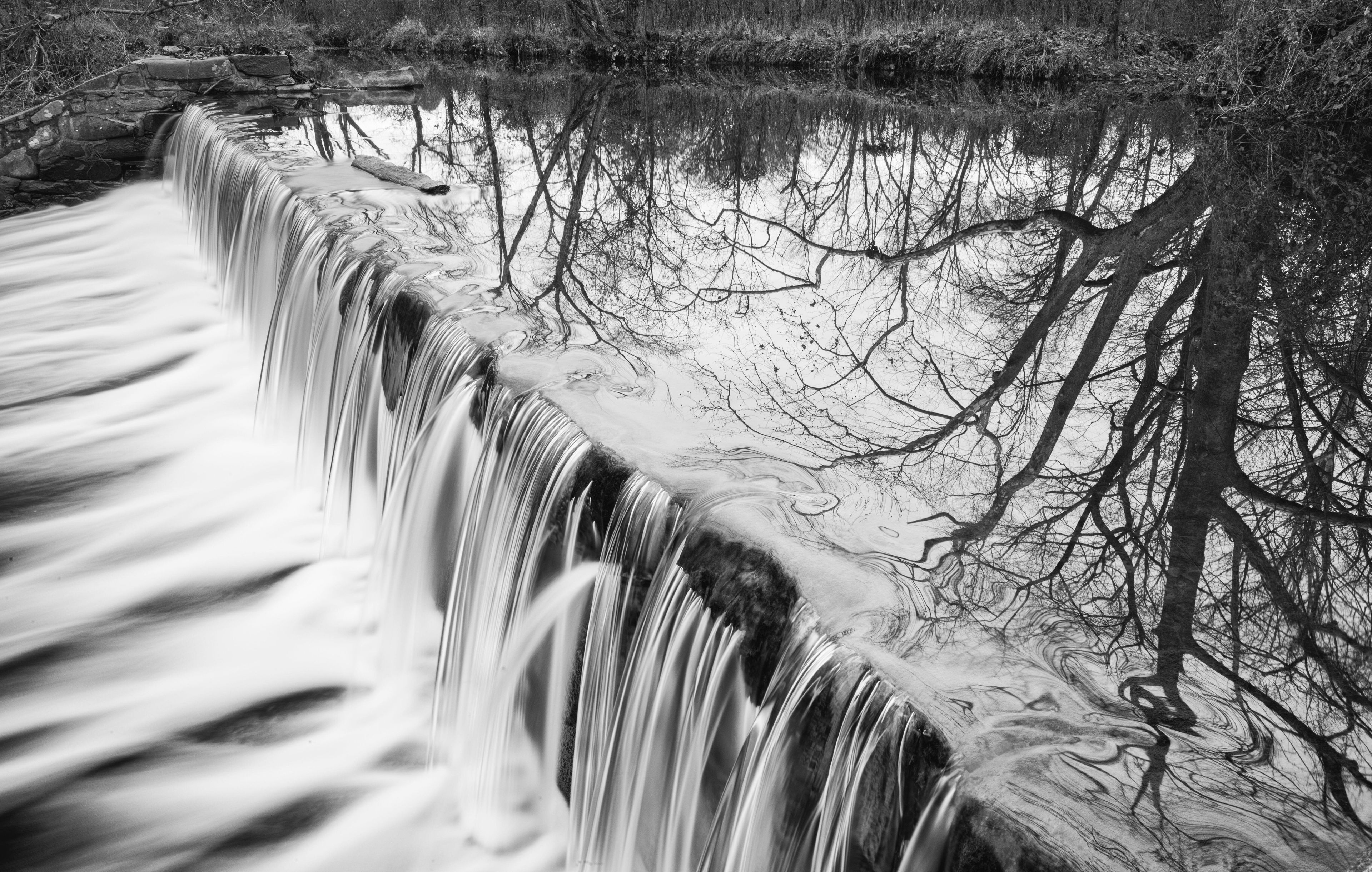 Una cascata che si getta su una barriera di pietra, con alberi spogli sullo sfondo.