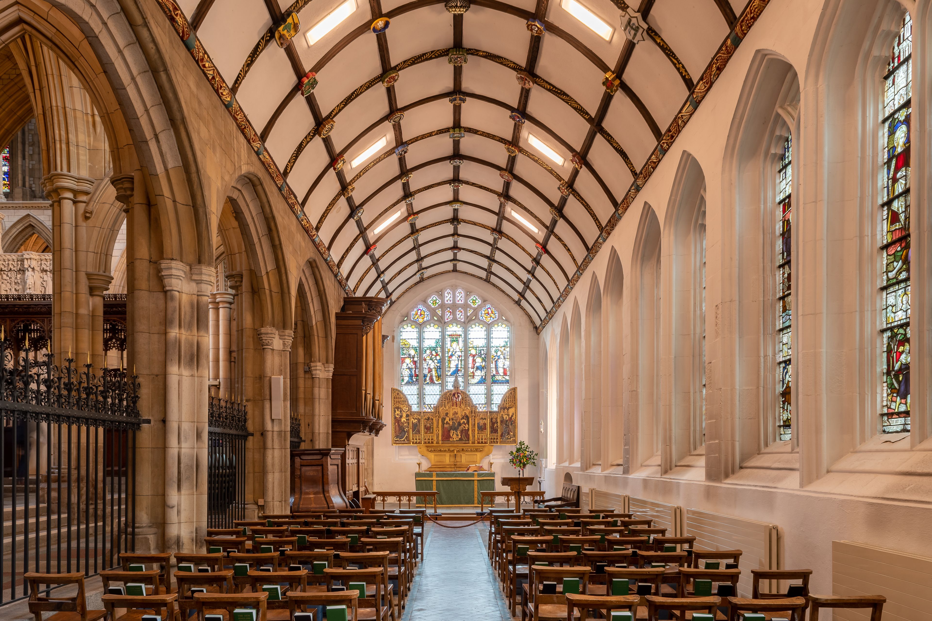 Ein Kircheninneres mit einer hohen gewölbten Decke, Buntglasfenstern und Reihen aus hölzernen Kirchenbänken.