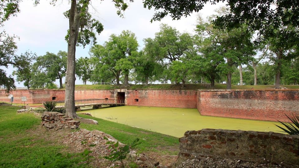 A historic fort with brick walls, a green lawn, and trees.