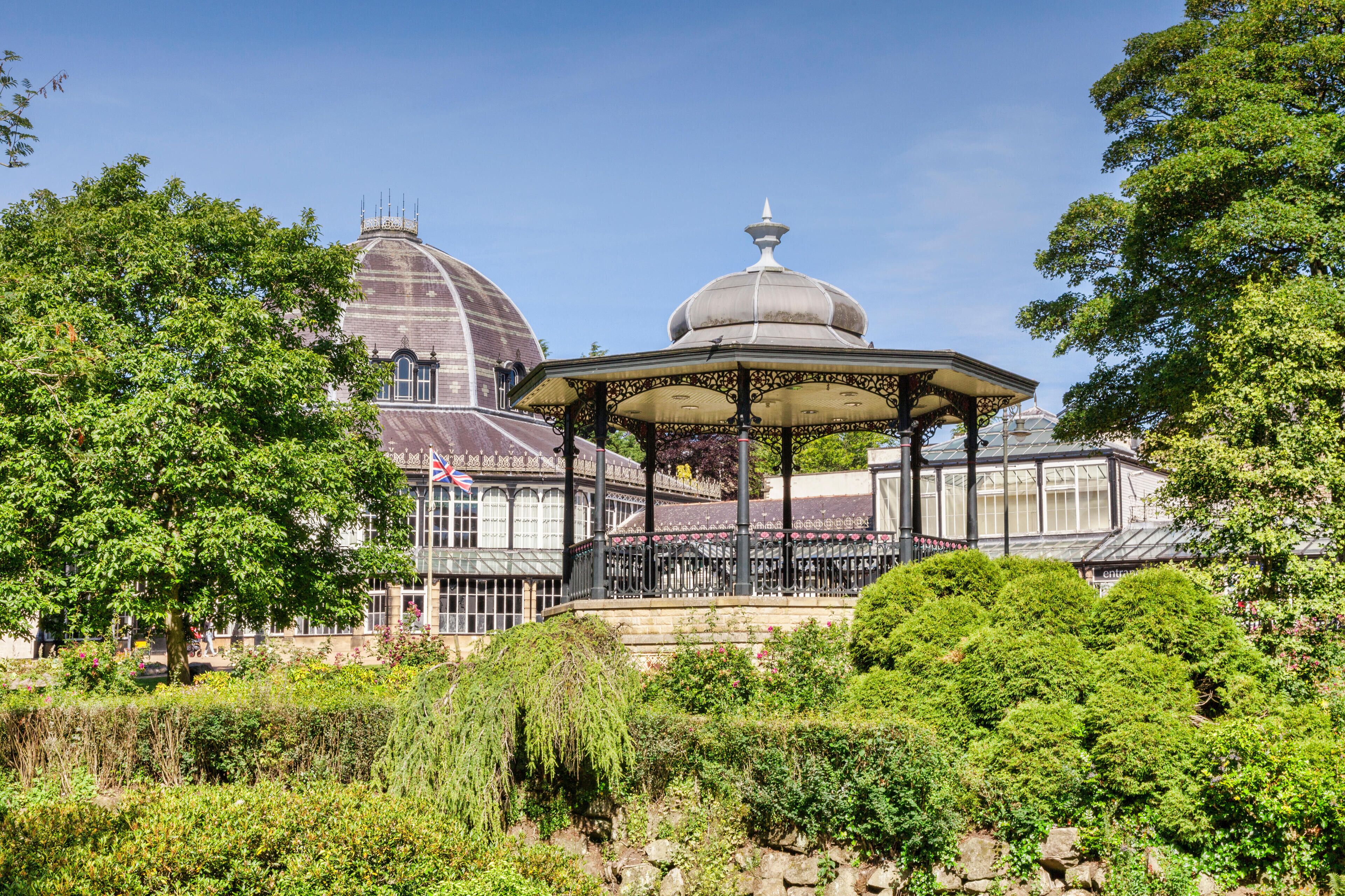 A gazebo surrounded by lush greenery, a large building with a dome, and a flagpole with a flag.