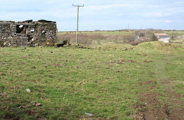 A stone ruin, a grassy field, and a utility pole in a rural landscape.