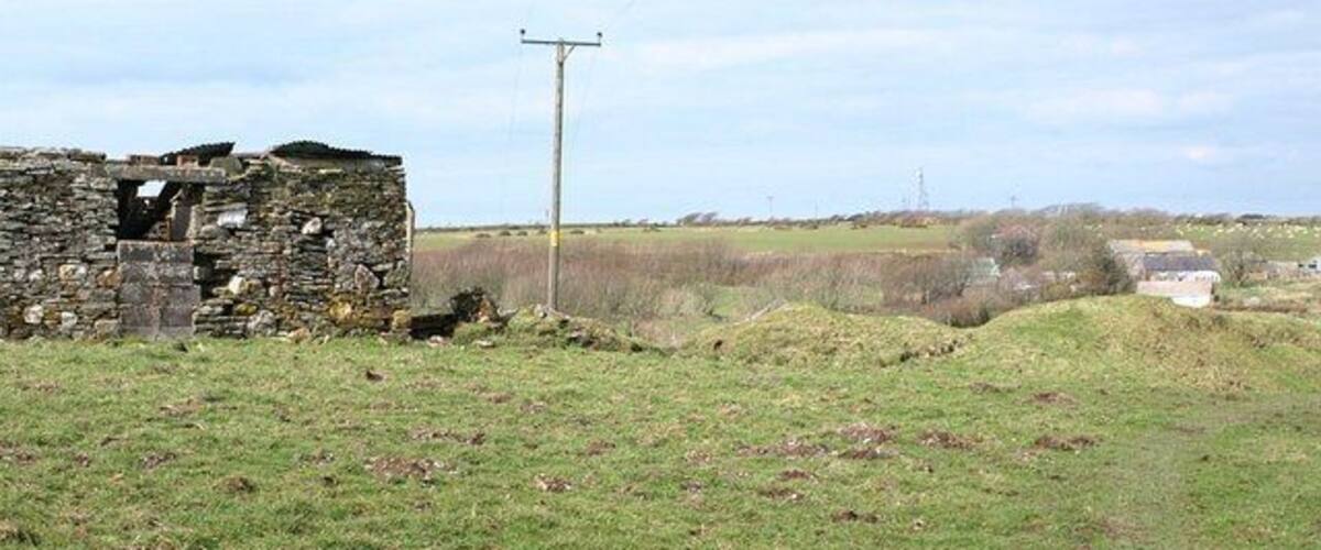 A stone ruin, a grassy field, and a utility pole in a rural landscape.