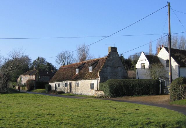 A rural village with stone houses, a clear sky, and a green field.
