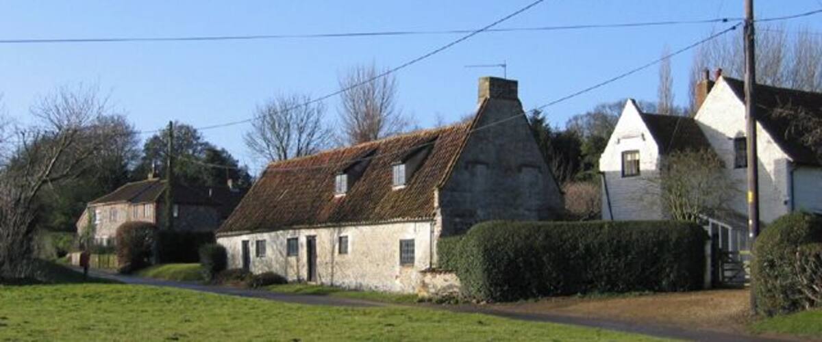 A rural village with stone houses, a clear sky, and a green field.