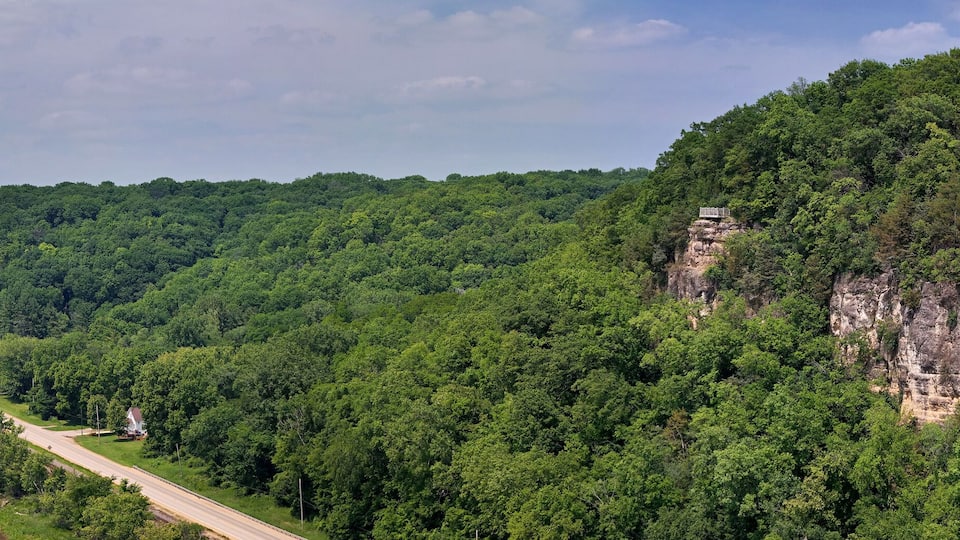 A river winding through a forested valley with a road running alongside it and a steep cliff on the right.