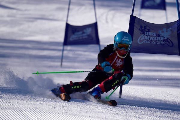 Un skieur en mouvement sur une pente enneigée, avec des drapeaux et un logo.