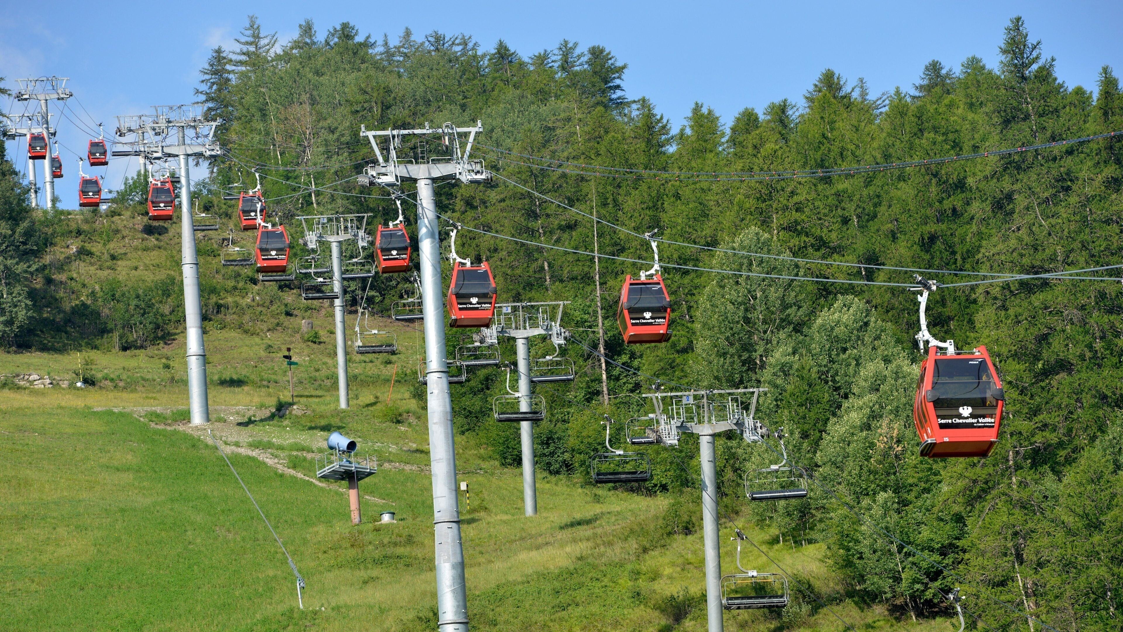 A cable car system with red gondolas ascending a mountain.
