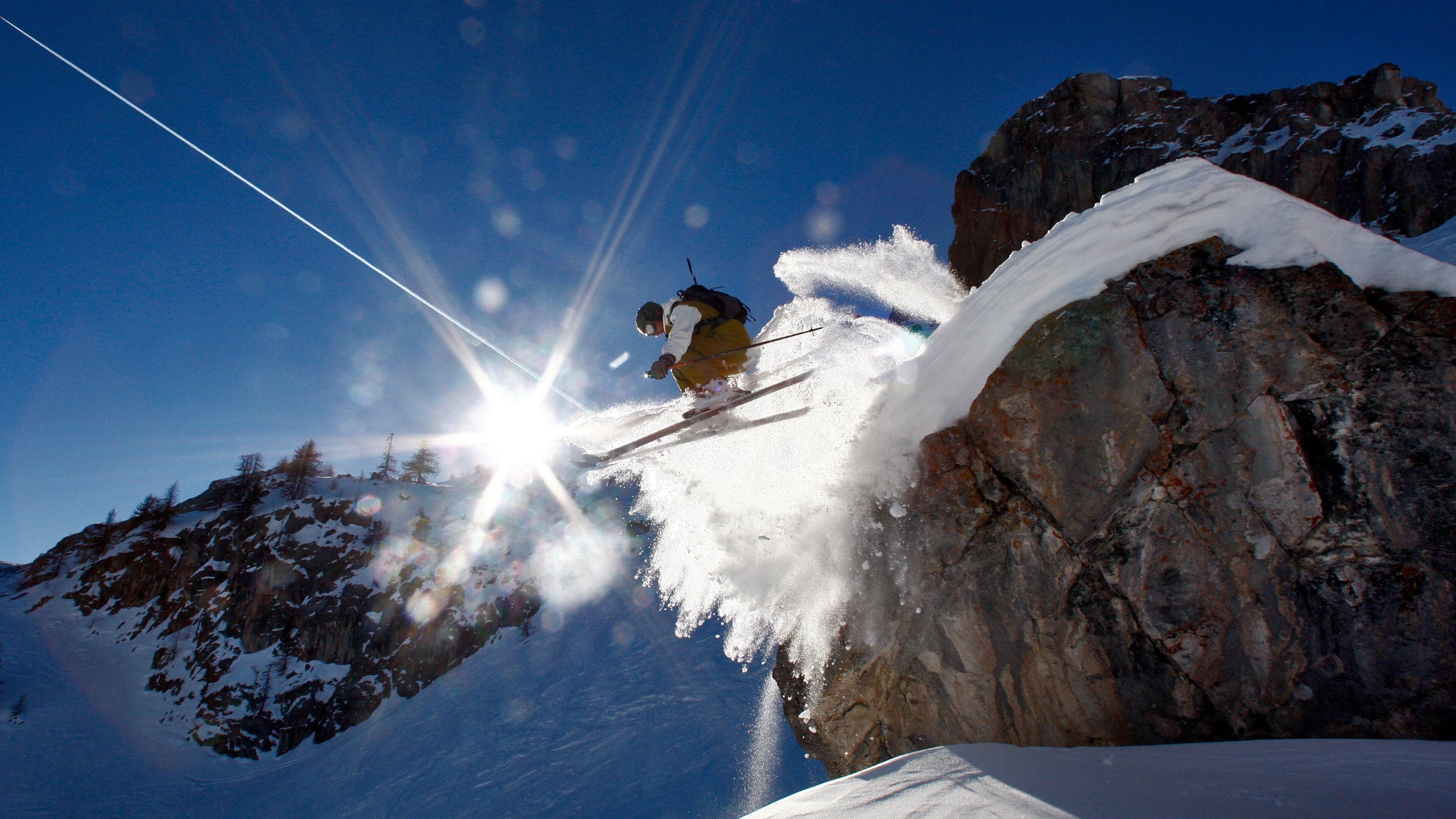A skier mid-jump over a snow-covered rock.