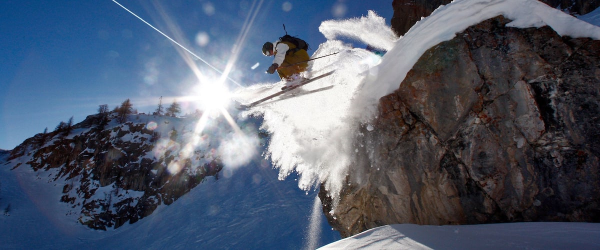 A skier mid-jump over a snow-covered rock.