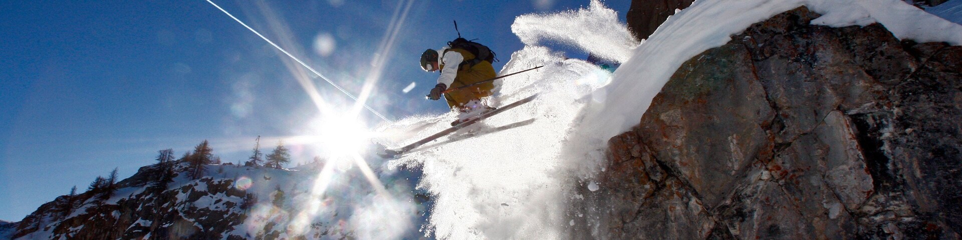 A skier mid-jump over a snow-covered rock.