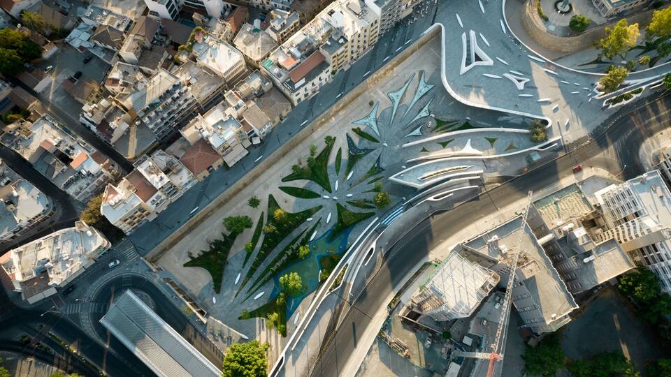 An aerial view of a city with a distinctive modern art installation in the center, surrounded by urban buildings and roads.