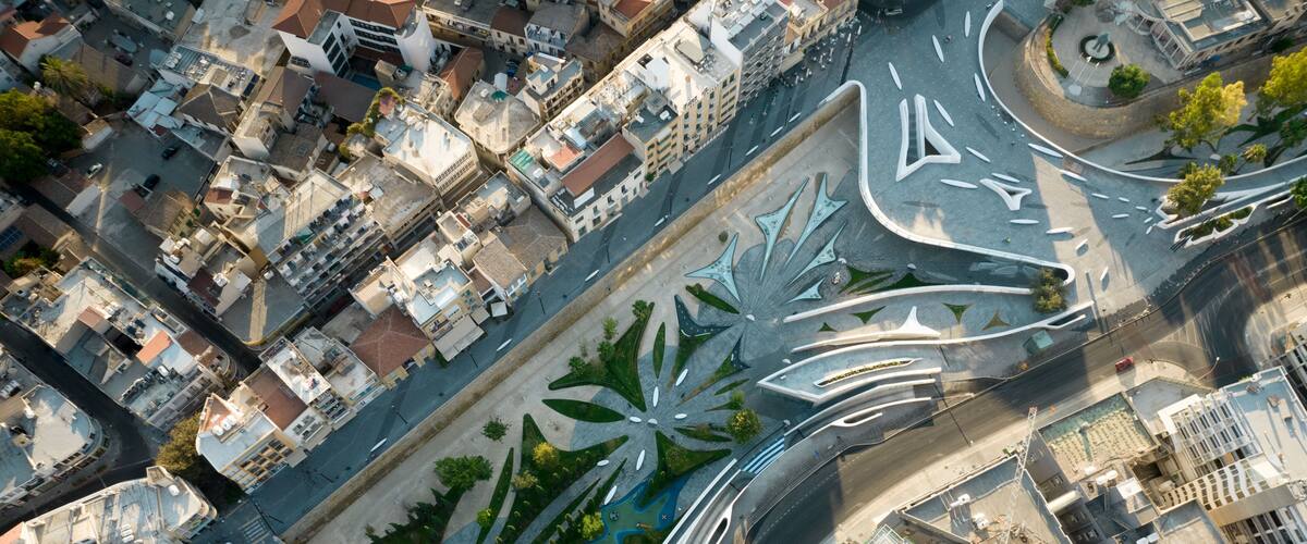 An aerial view of a city with a distinctive modern art installation in the center, surrounded by urban buildings and roads.