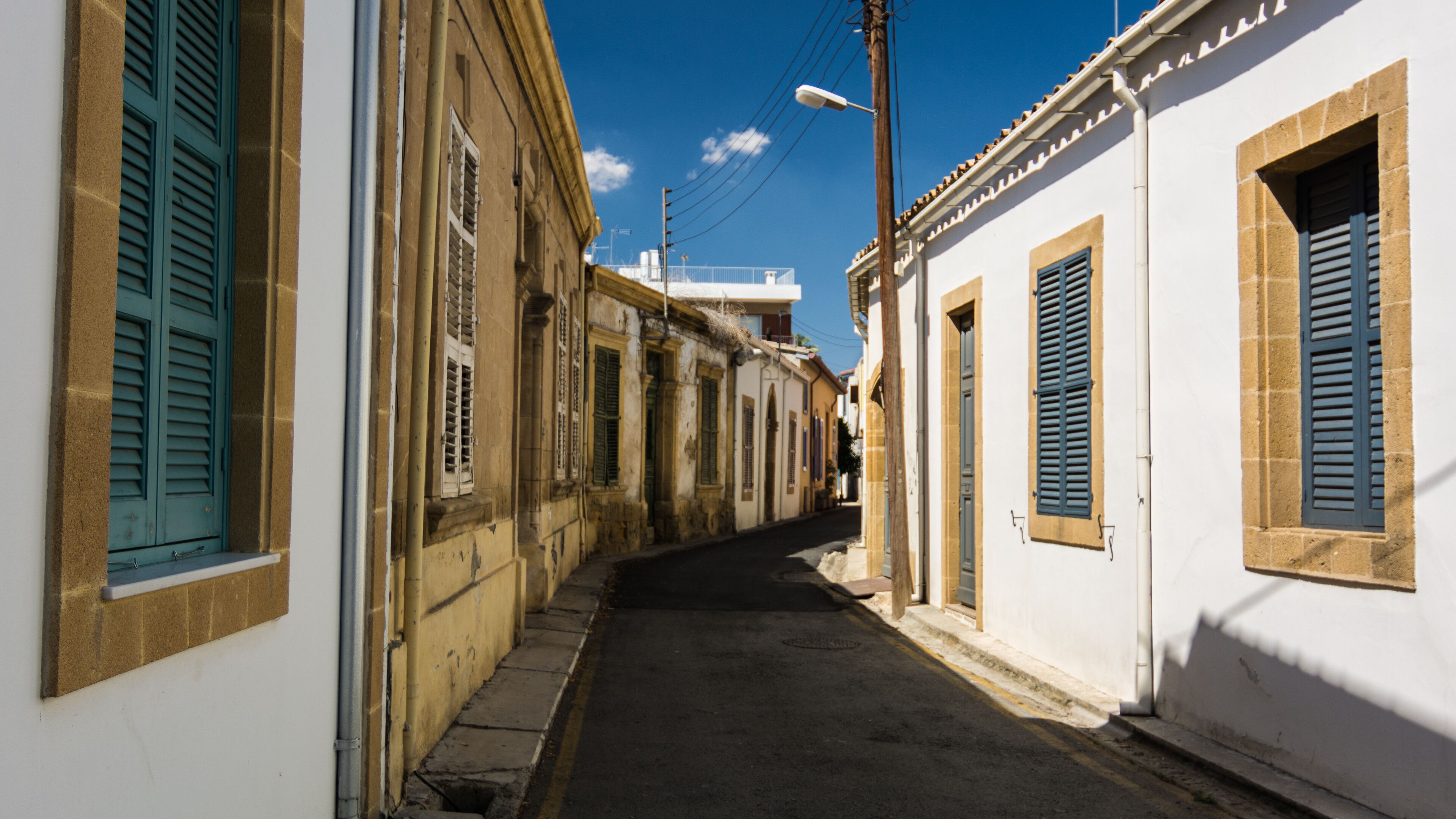 A narrow street flanked by buildings with shutters, under a clear sky.