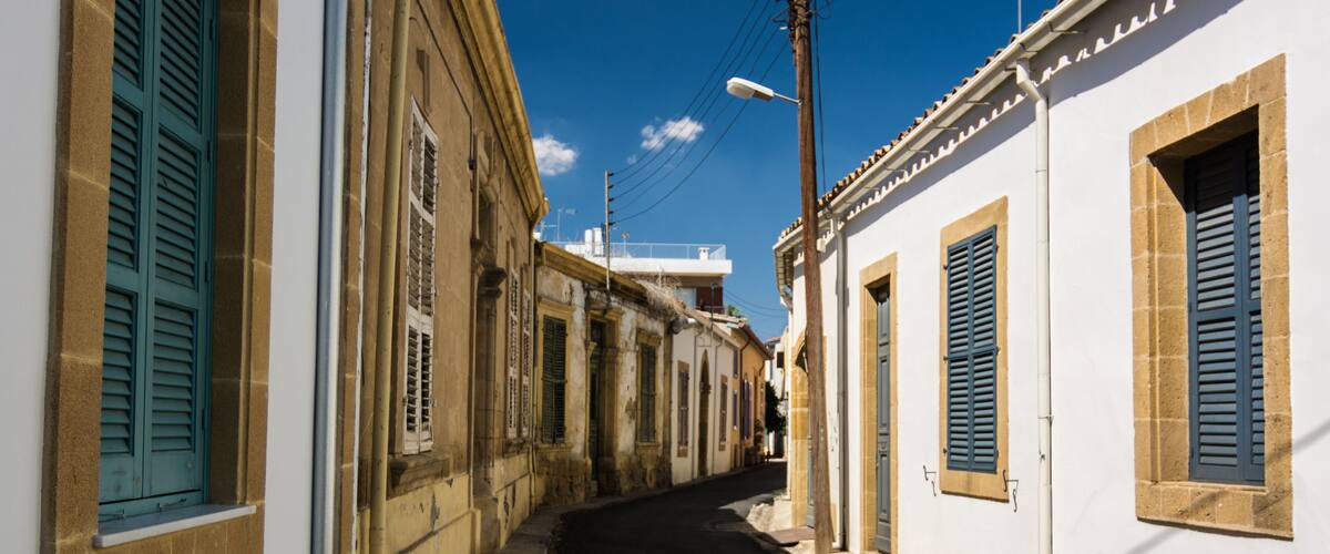 A narrow street flanked by buildings with shutters, under a clear sky.