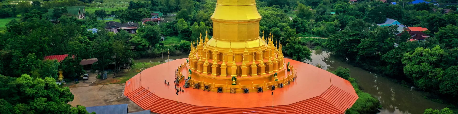 Una estupa dorada rodeada de exuberante vegetación y un río.
