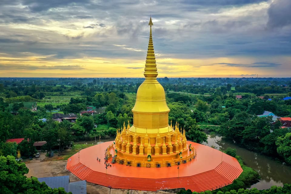 A golden stupa surrounded by lush greenery and a river.