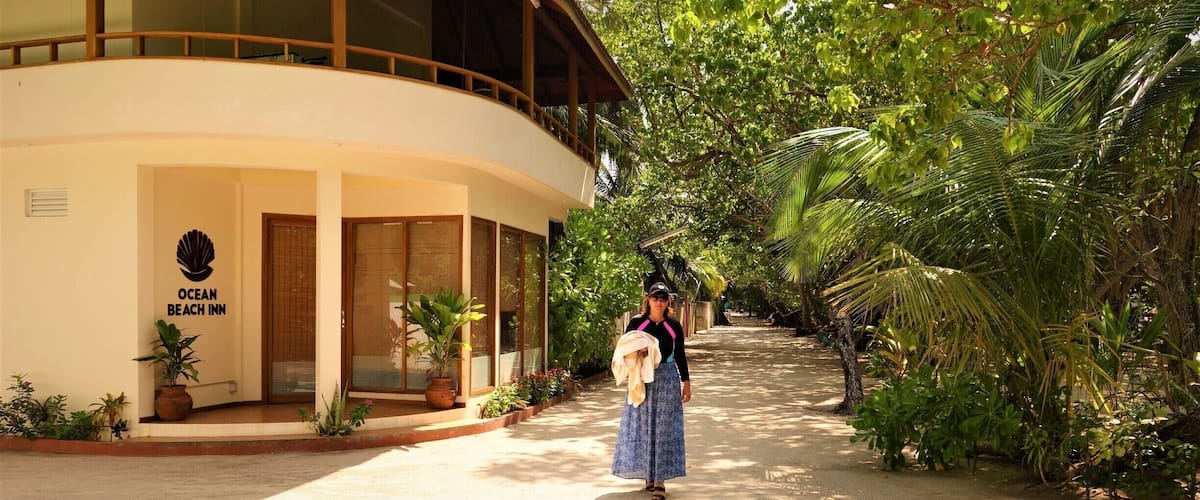 A pathway leading to a building labeled "Ocean Beach Inn," surrounded by lush greenery and palm trees.