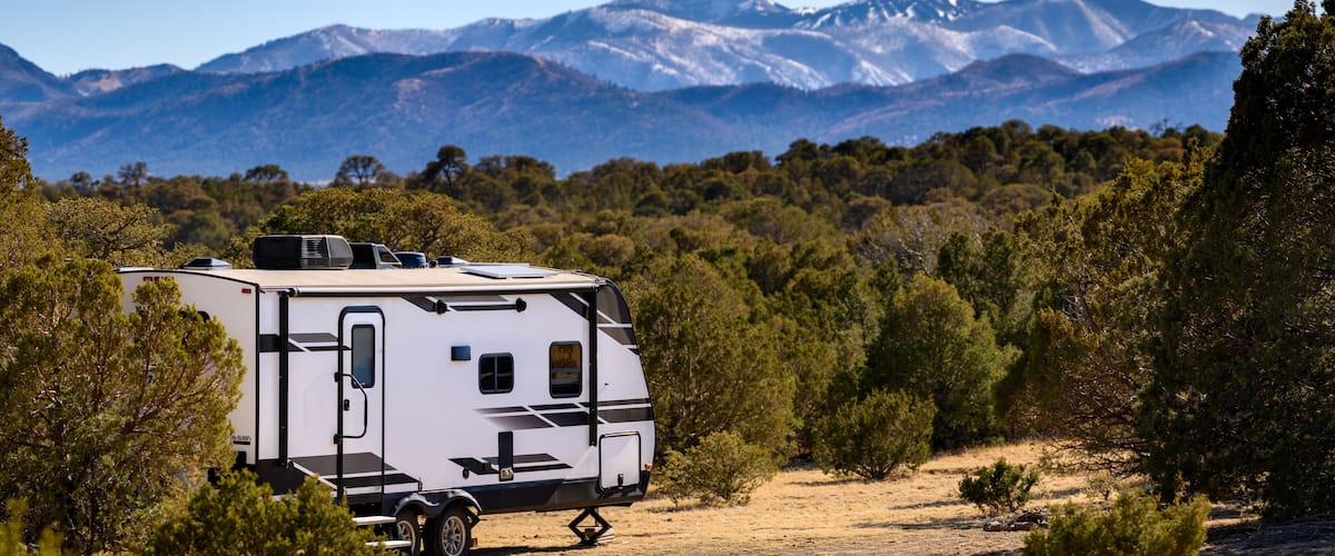 A white RV parked in a forested area with mountains in the background.
