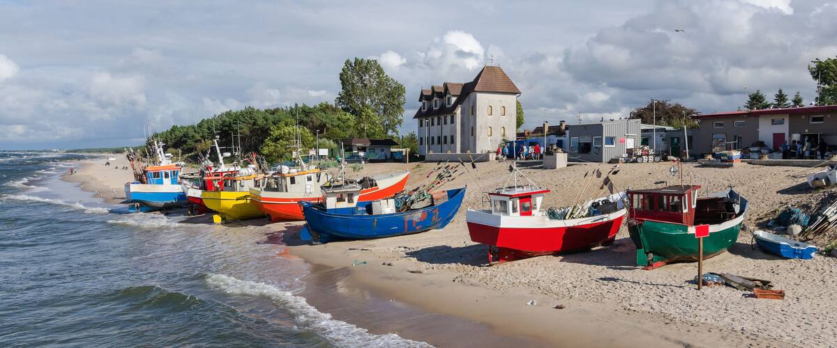 A beach with colorful boats, a large house, and a sandy shore.