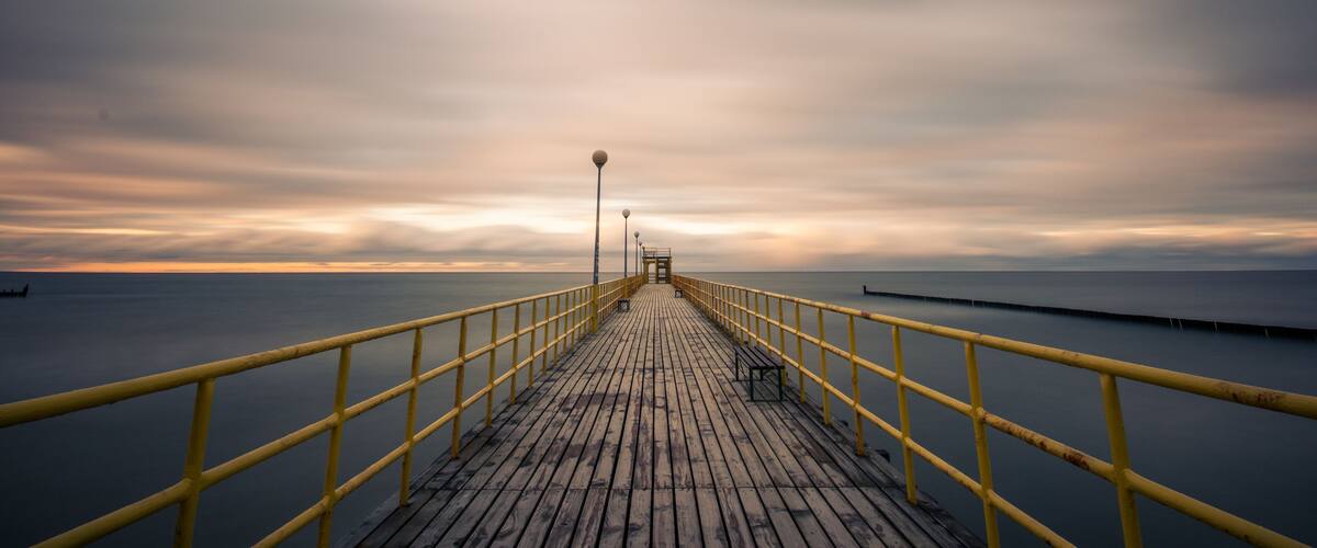 A wooden pier extending into calm waters under a cloudy sky.
