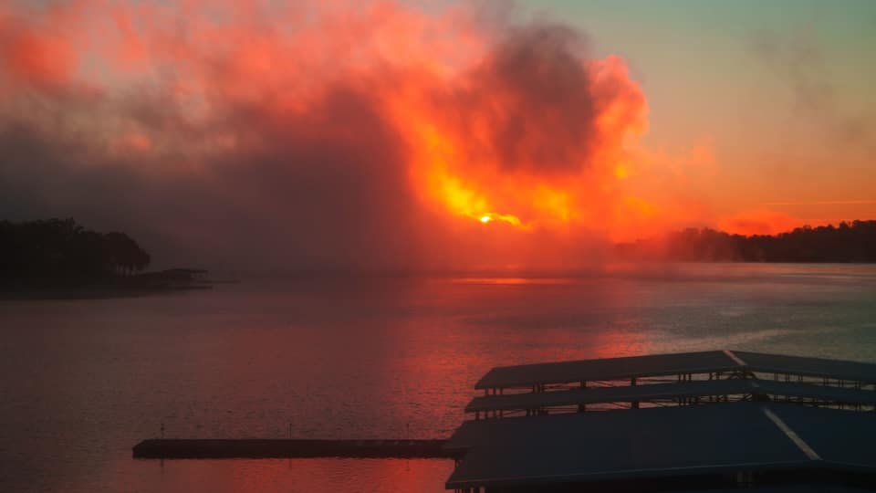 A sunset over a body of water with a dock and a distant shoreline.