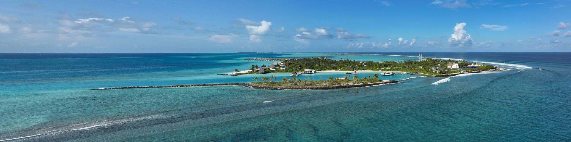 Aerial view of a serene island fringed by turquoise waters, showcasing a vibrant contrast between the lush greenery and the clear blue sky, Thulusdhoo, Kaafu Atoll, Maldives.