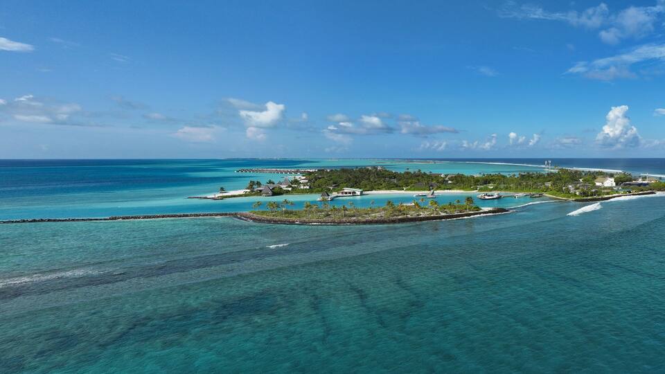Aerial view of a serene island fringed by turquoise waters, showcasing a vibrant contrast between the lush greenery and the clear blue sky, Thulusdhoo, Kaafu Atoll, Maldives.