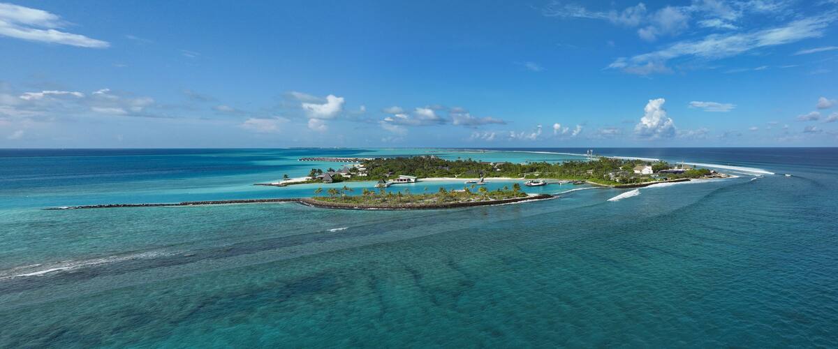 A tropical island with clear turquoise waters, a small pier, and lush greenery.