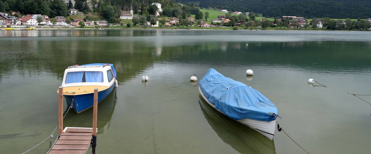 A lake with two boats docked, a wooden pier, and houses in the background.