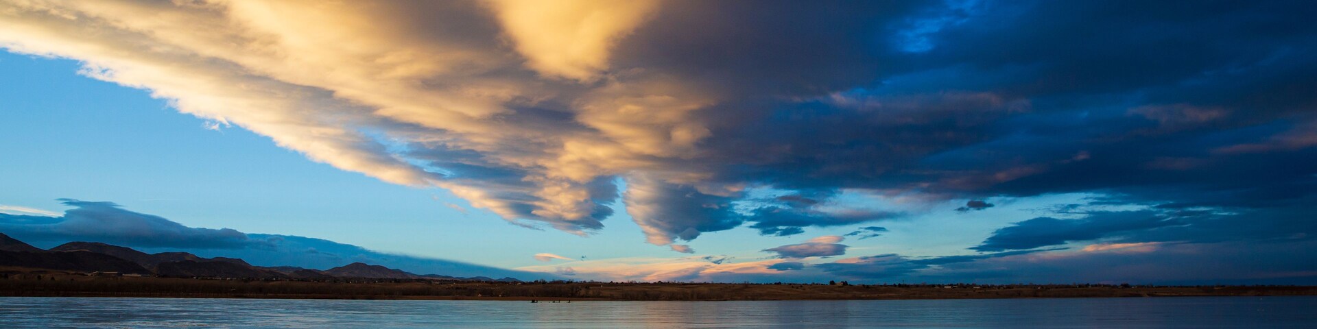 Um pôr do sol sobre um lago calmo, com montanhas ao fundo.