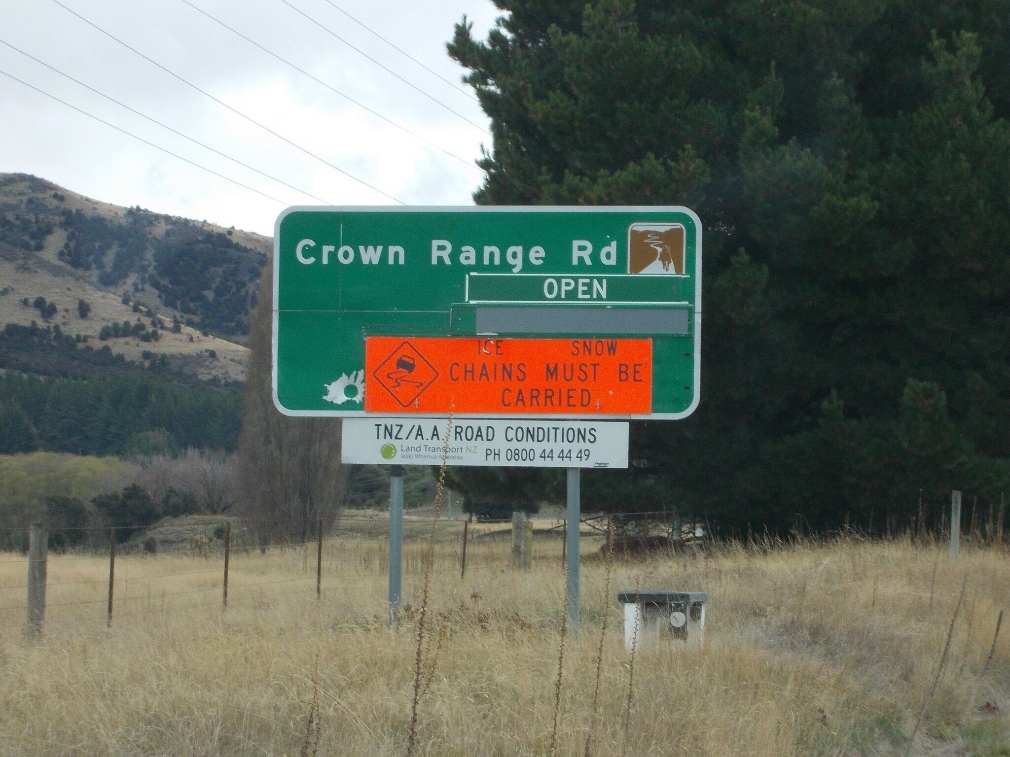 A road sign for Crown Range Rd with an open road symbol and a warning about snow chains.