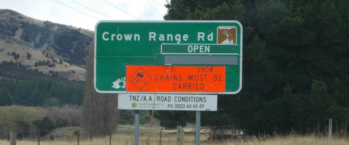 A road sign for Crown Range Rd with an open road symbol and a warning about snow chains.