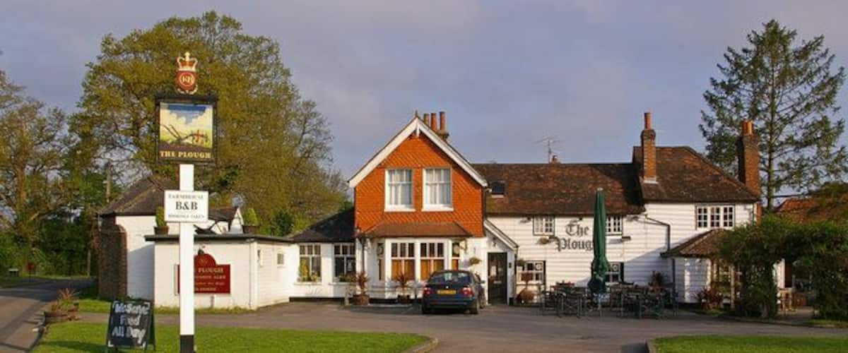 A traditional pub with a red-tiled roof, a signboard, and a car parked in front.
