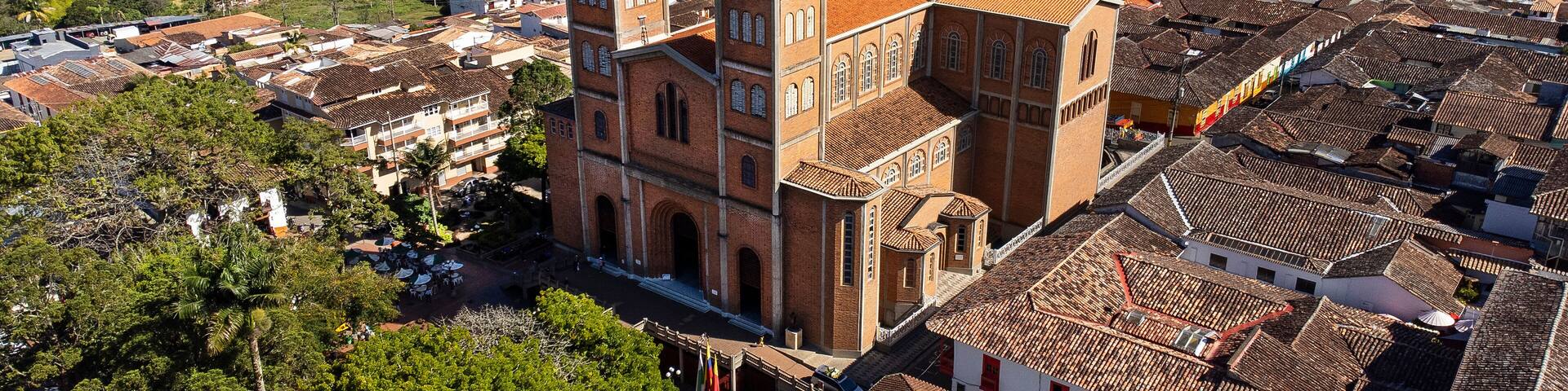 Una iglesia histórica con una torre del reloj, rodeada de casas escalonadas y exuberante vegetación.