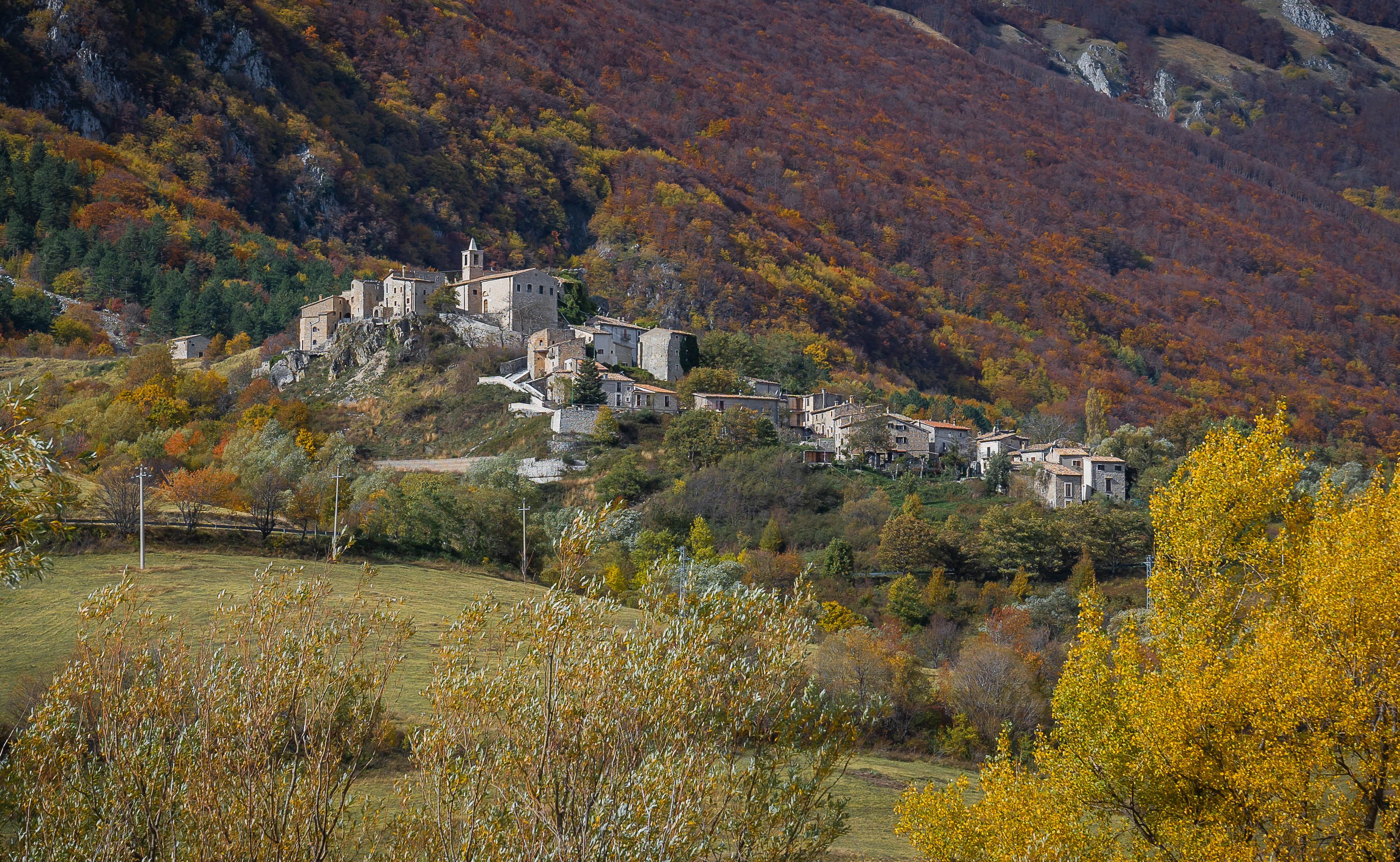 A hillside village with stone buildings and autumn foliage.