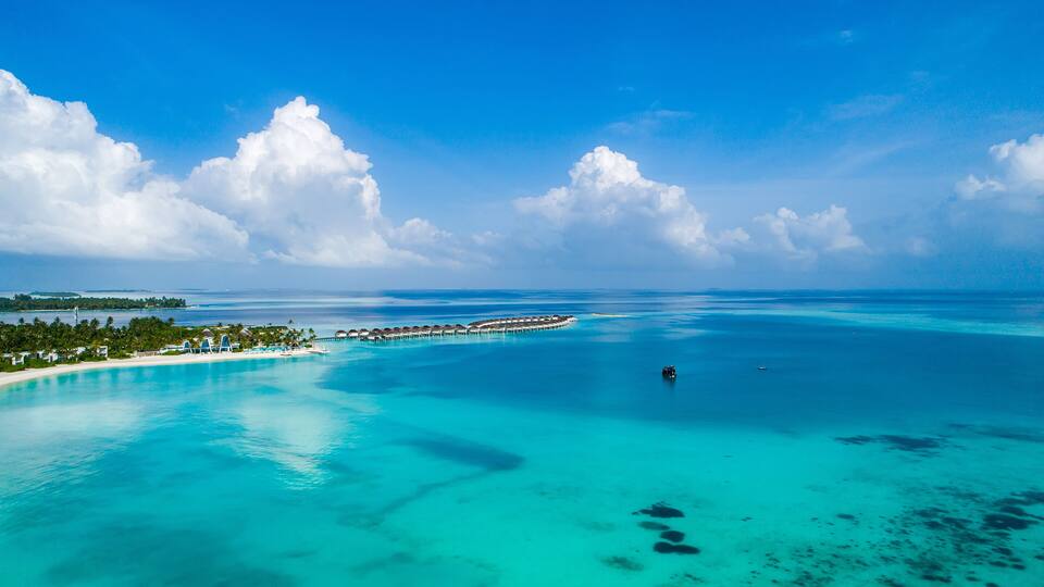 A tropical island with clear turquoise waters, a long pier, and lush greenery.