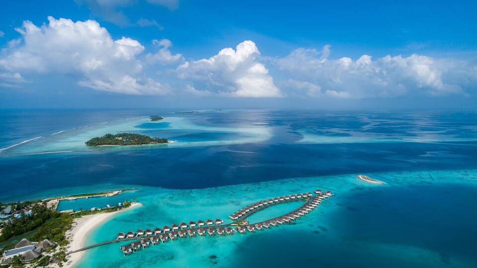 An aerial view of a tropical island resort with overwater bungalows and clear turquoise waters.